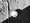 Schwarz-weißes Bild: Ein weißer Ball und ein dünner Ast liegen auf einem kiesigen Boden. Ein diagonal verlaufender Schatten teilt die Szene in helles Licht und Dunkelheit.