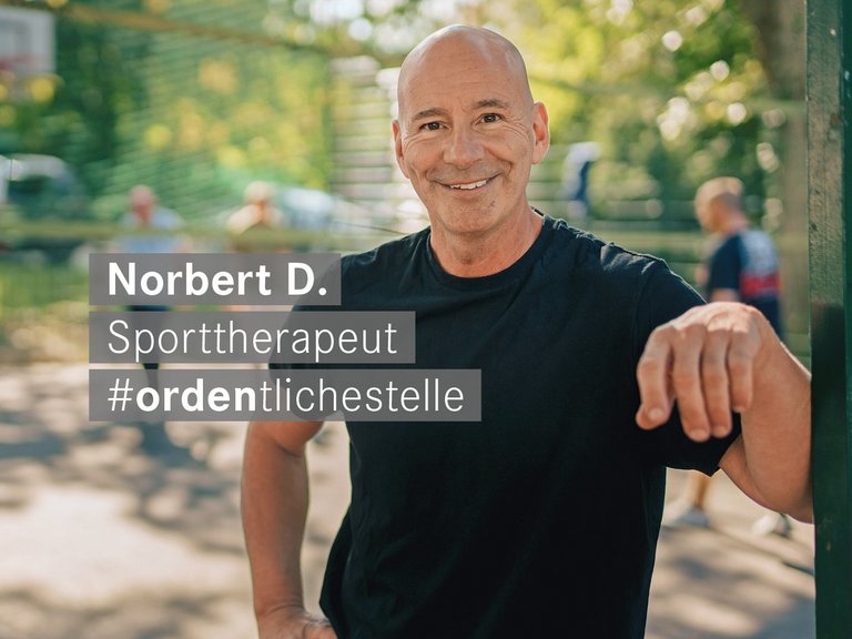 Ein lächelnder Mann in einem schwarzen T-Shirt lehnt an einem Pfosten. Ein Textfeld identifiziert ihn als Norbert D., Sporttherapeut, und zeigt den Hashtag #ordentlichestelle.